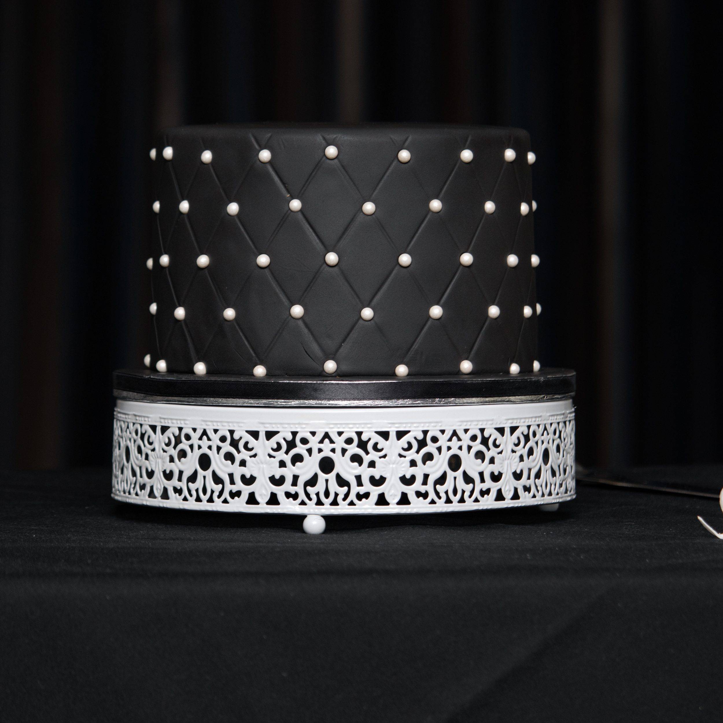 The wedding cake, black with fairy lights behind it